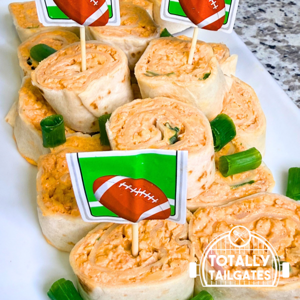 Tailgate appetizer Buffalo Chicken Pinwheels are on a white platter with football themed cupcake toppers.